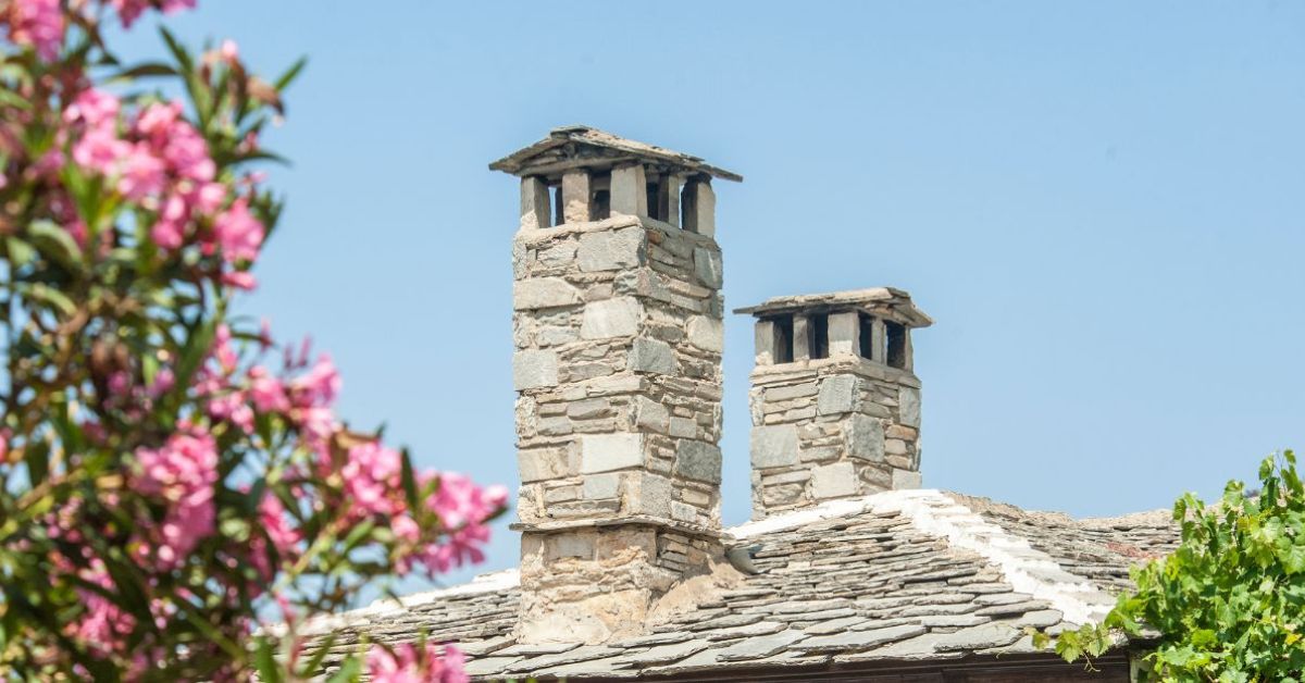 two-brick-chimneys-behind-flowers-when-is-the-best-time-to-get-my-chimney-repaired-den-defenders