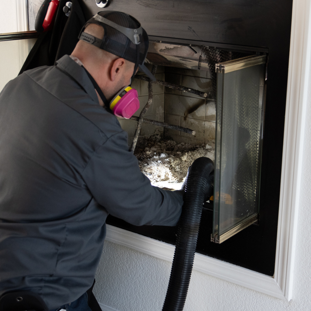 Den Defenders Chimney technician vacuuming soot and debris from a fireplace during chimney cleaning